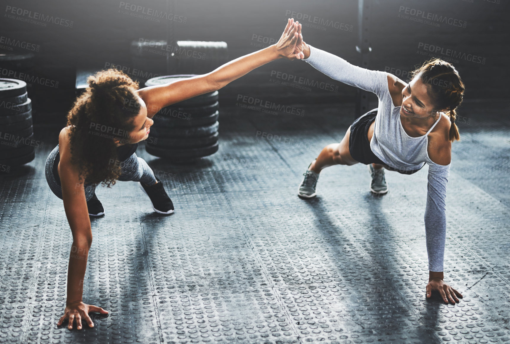 Buy stock photo Shot of two young women giving each other a high five while doing push ups at the gym