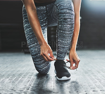 Buy stock photo Cropped shot of a woman tying her shoelaces in a gym