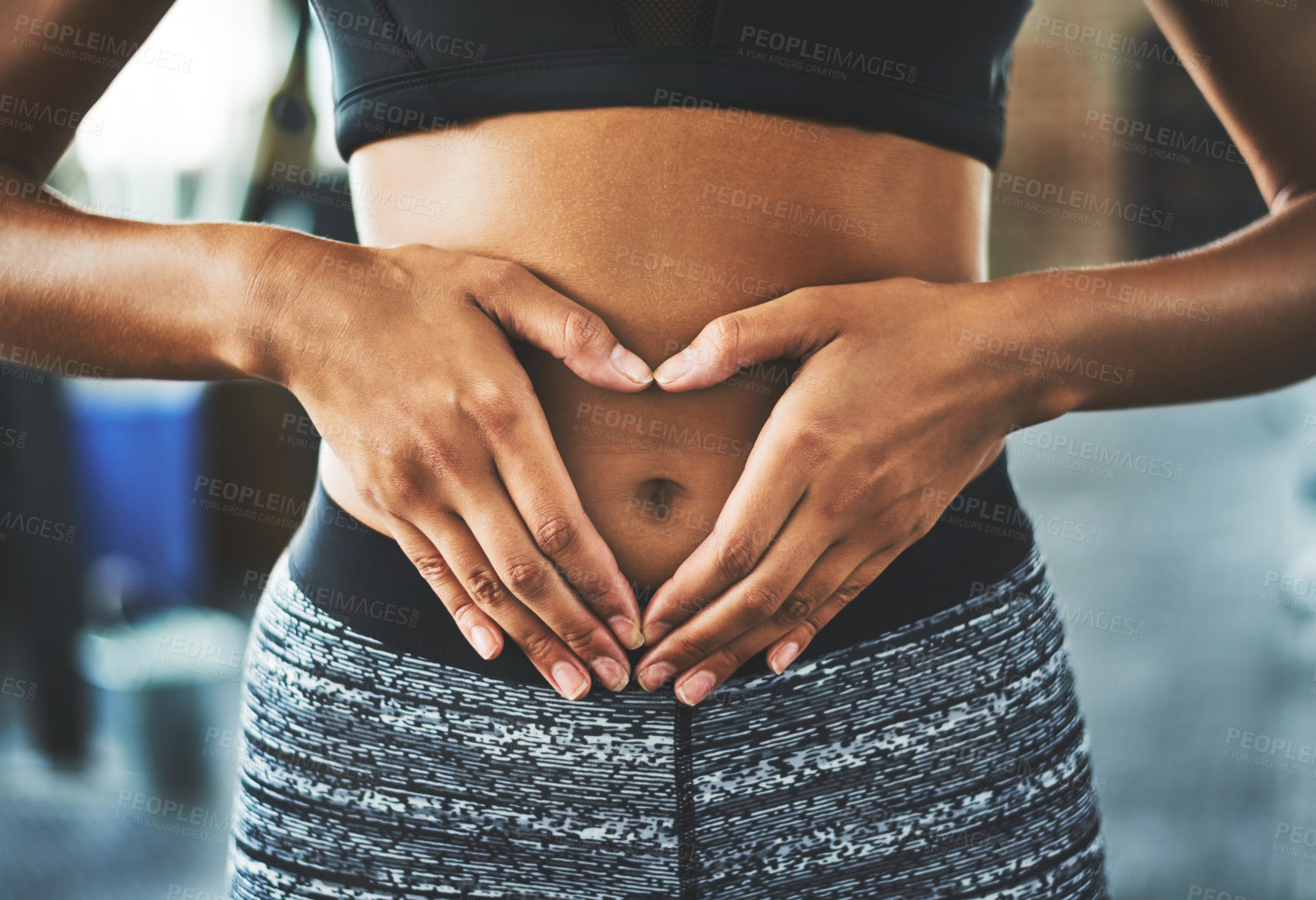 Buy stock photo Cropped shot of a fit young woman making a heart shaped gesture over her stomach in a gym