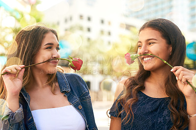 Buy stock photo Cropped shot of two female best friends being playful with roses in the city
