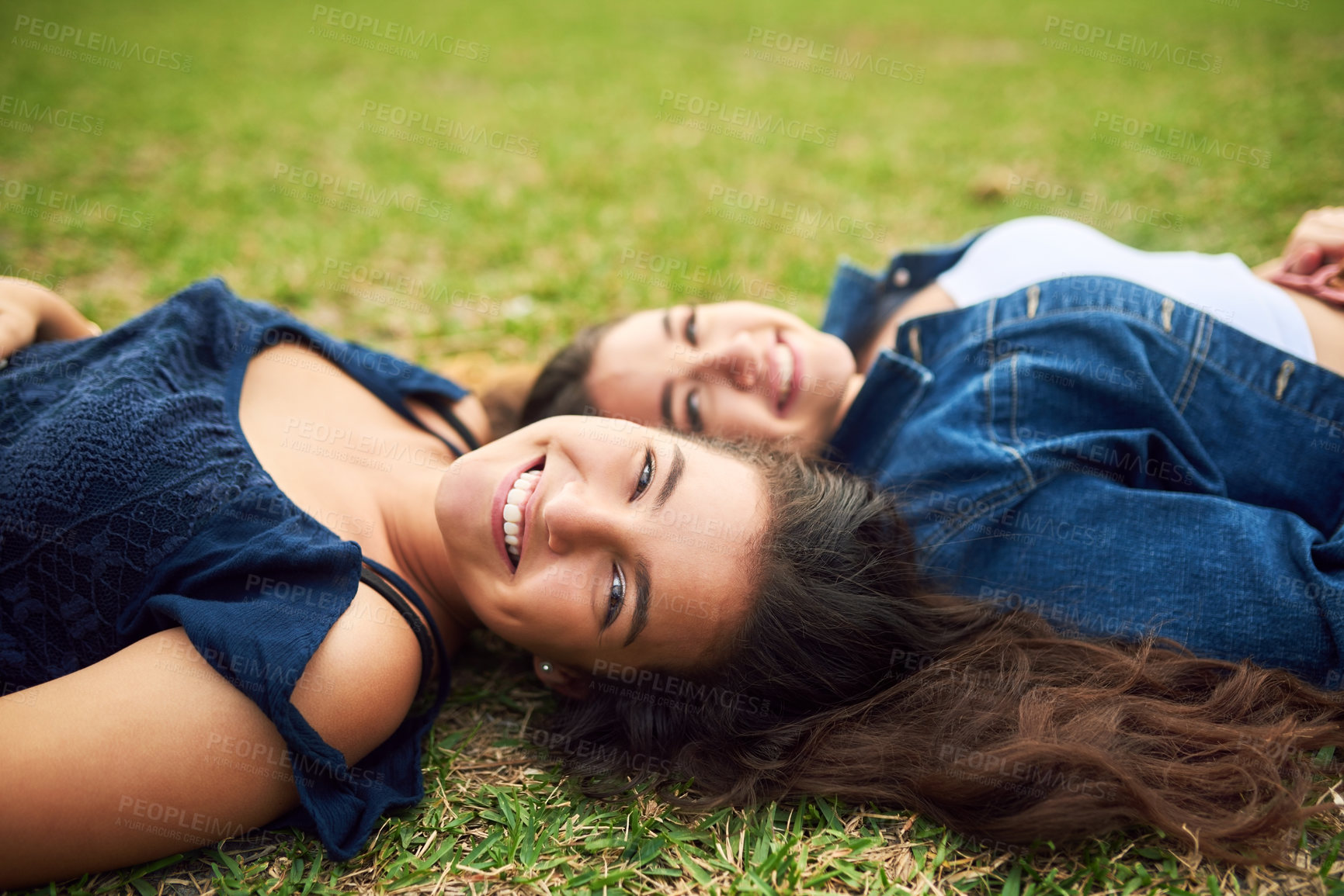 Buy stock photo Cropped shot of two female best friends lying on the grass in a public park