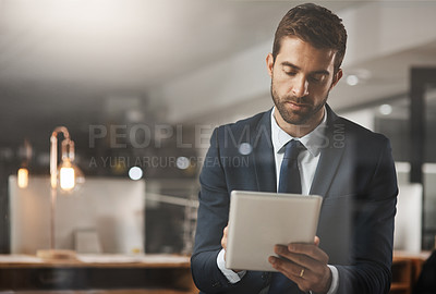 Buy stock photo Shot of a young businessman using a digital tablet while working late in an office