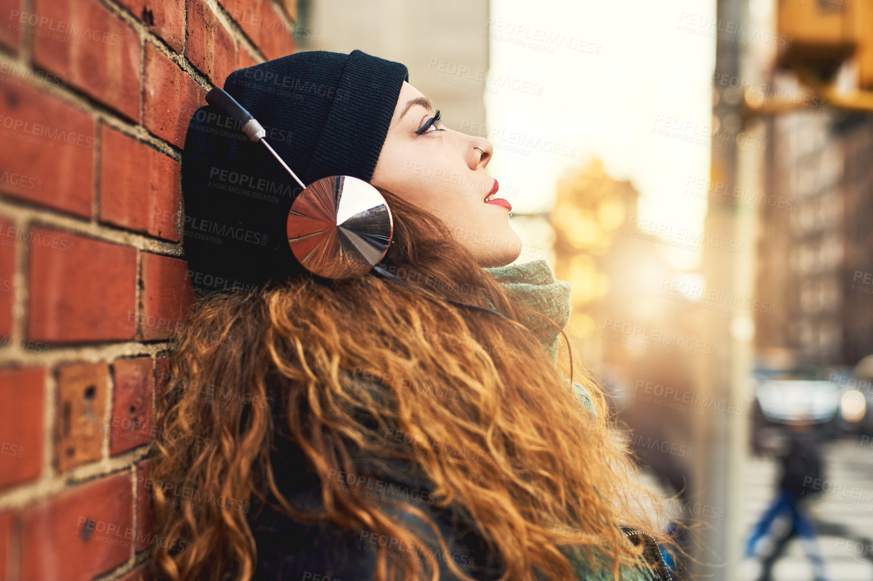 Buy stock photo Cropped shot of a young woman listening to music while leaning against a brick wall outside