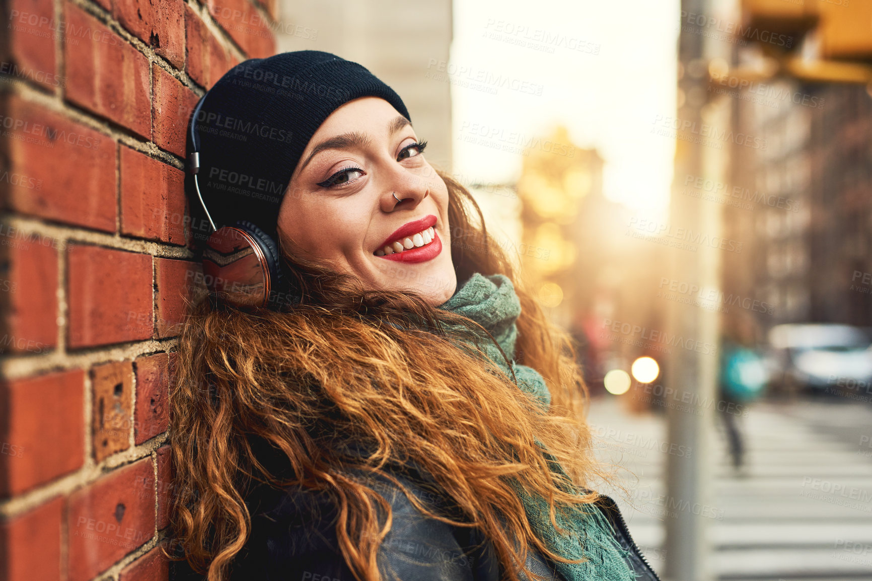 Buy stock photo Cropped shot of a young woman listening to music while leaning against a brick wall outside