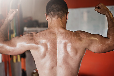 Buy stock photo Rearview shot of an unrecognizable muscular young man showing off his biceps in the gym