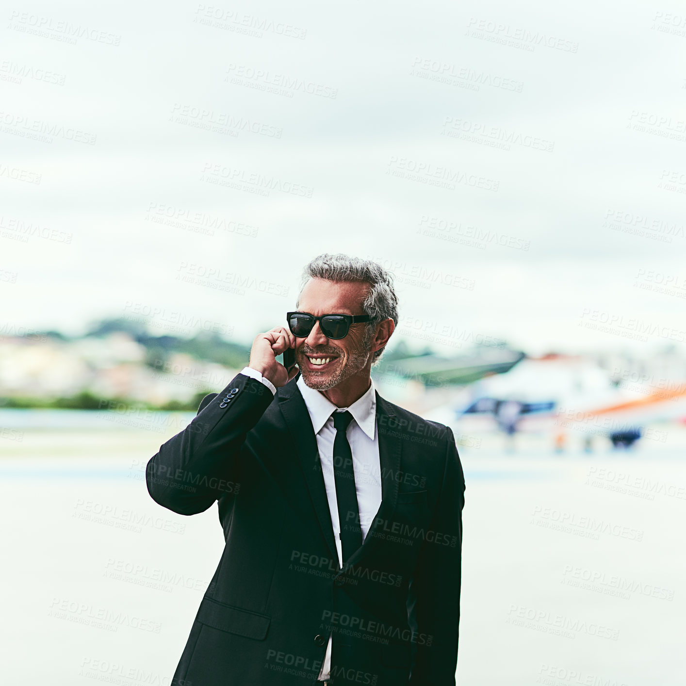 Buy stock photo Cropped shot of a handsome mature businessman talking on his cellphone while walking outside of the airport