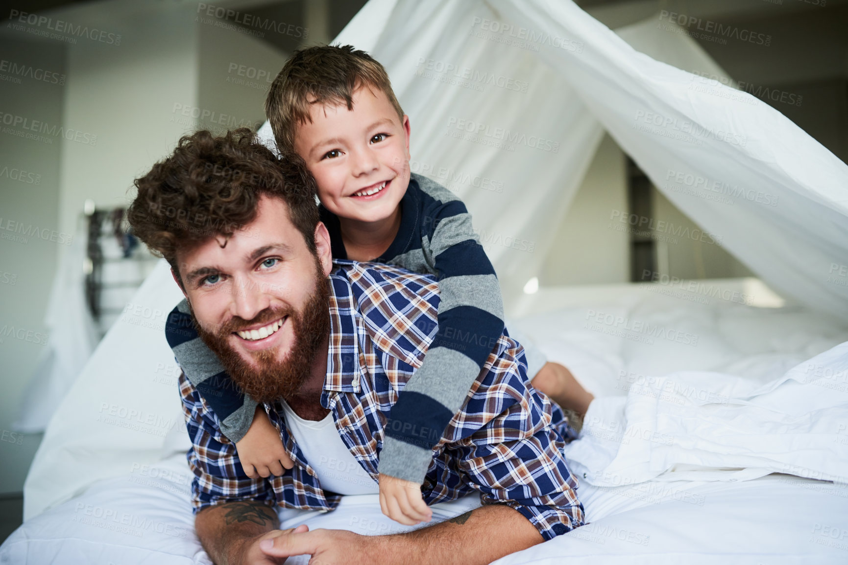 Buy stock photo Cropped portrait of a handsome young man lying on the bed at home with his son on his back