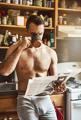 Buy stock photo Cropped shot of a handsome young shirtless man drinking a cup of coffee and reading the newspaper in the kitchen at home