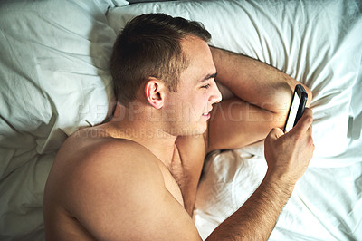 Buy stock photo Cropped shot of a young handsome shirtless man using a cellphone in bed at home