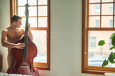 Buy stock photo Cropped shot of a young handsome shirtless man playing the cello and looking out the window at home