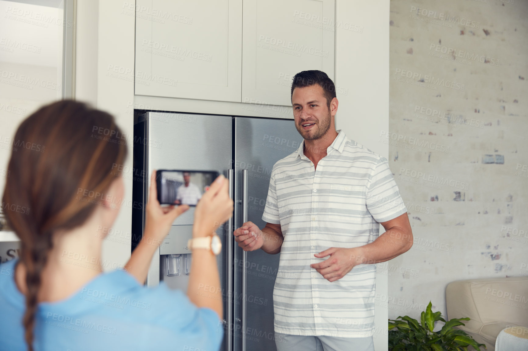 Buy stock photo Cropped shot of an unrecognizable woman taking a picture of her husband in the kitchen at home