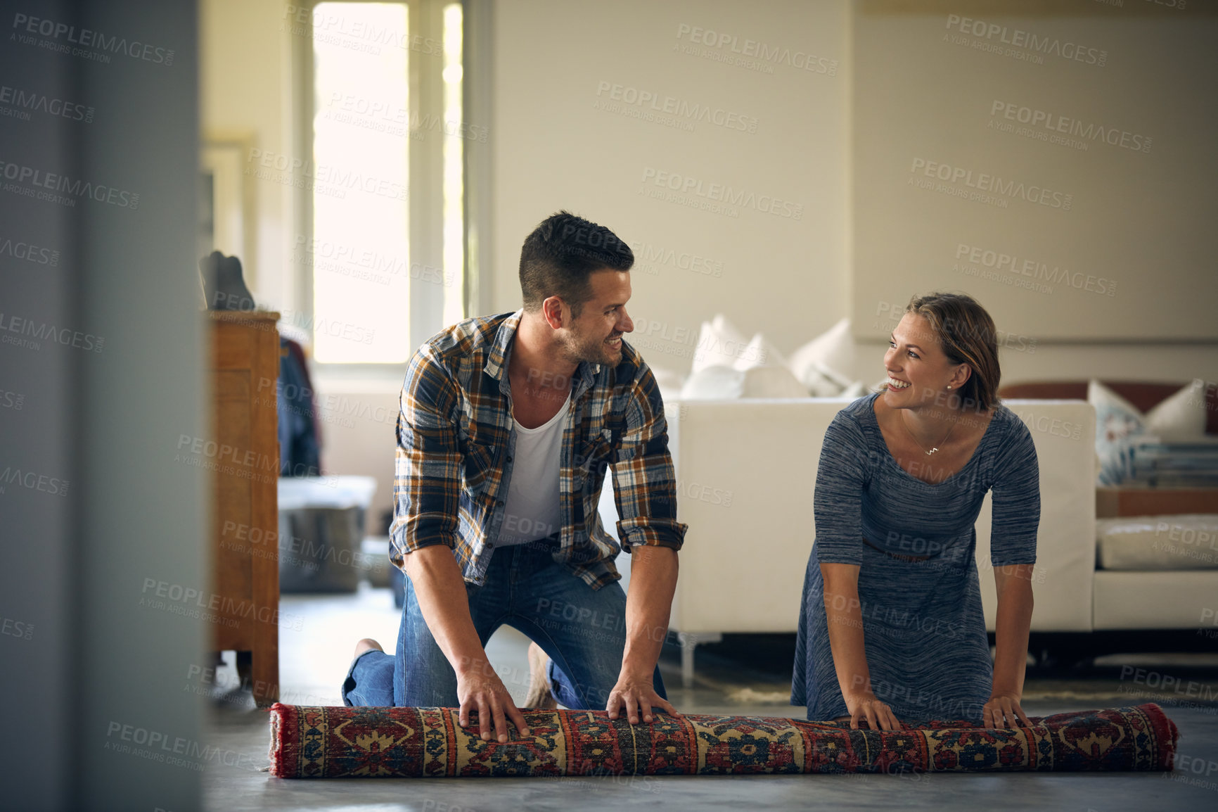 Buy stock photo Shot of a young married couple rolling up a carpet together at home