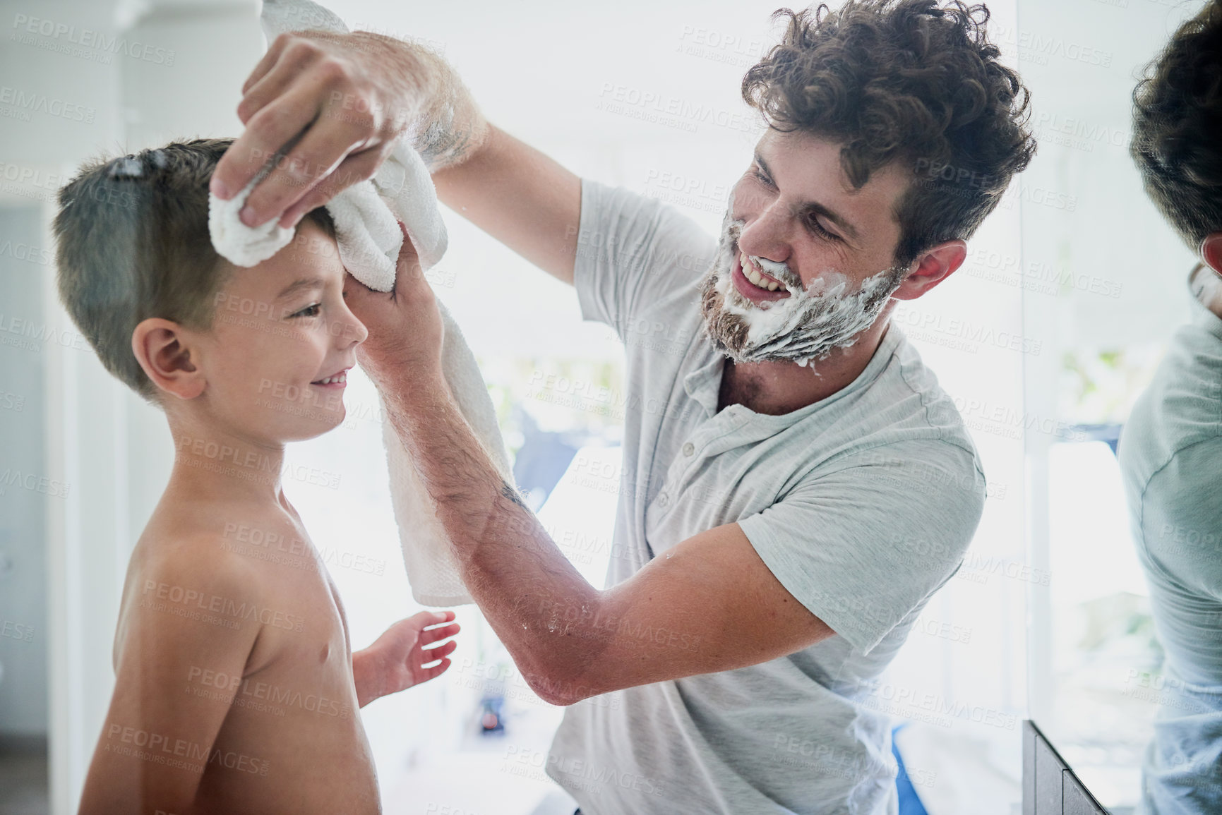 Buy stock photo Shot of a father wiping his son's face while shaving in the bathroom at home