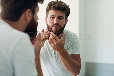 Buy stock photo Face, beauty and beard with a man in the bathroom of his home in the morning for fresh hygiene. Mirror, reflection and care with a handsome young male person checking his skin for facial treatment