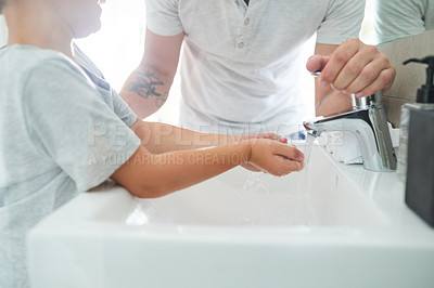 Buy stock photo Cropped shot of an unrecognizable father helping his adorable little boy wash his hands in the bathroom at home