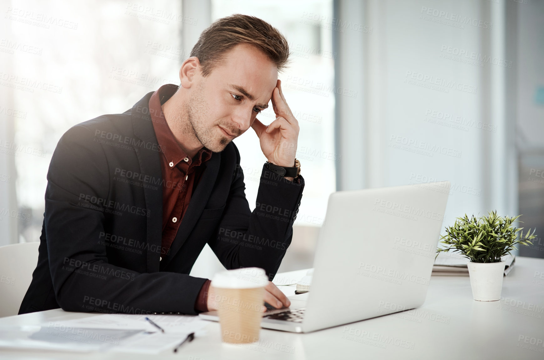 Buy stock photo Shot of a young businessman looking stressed out while working on a laptop in an office