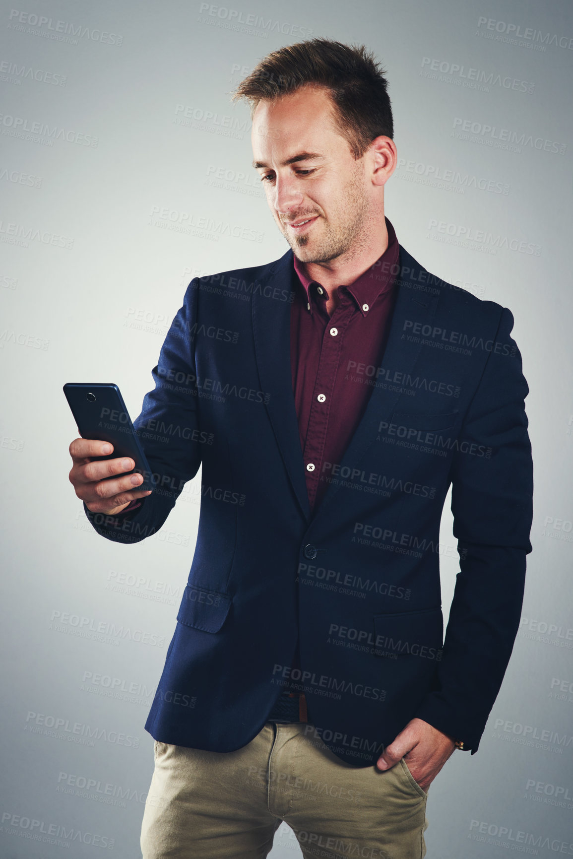 Buy stock photo Studio shot of a confident young businessman using a mobile phone against a gray background