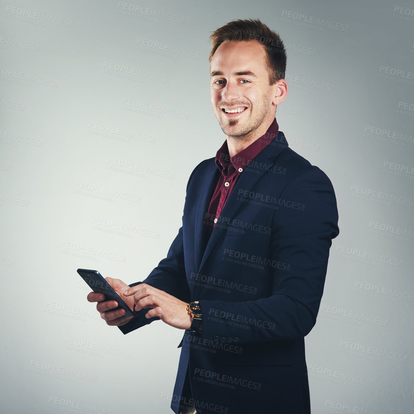 Buy stock photo Studio portrait of a confident young businessman using a mobile phone against a gray background