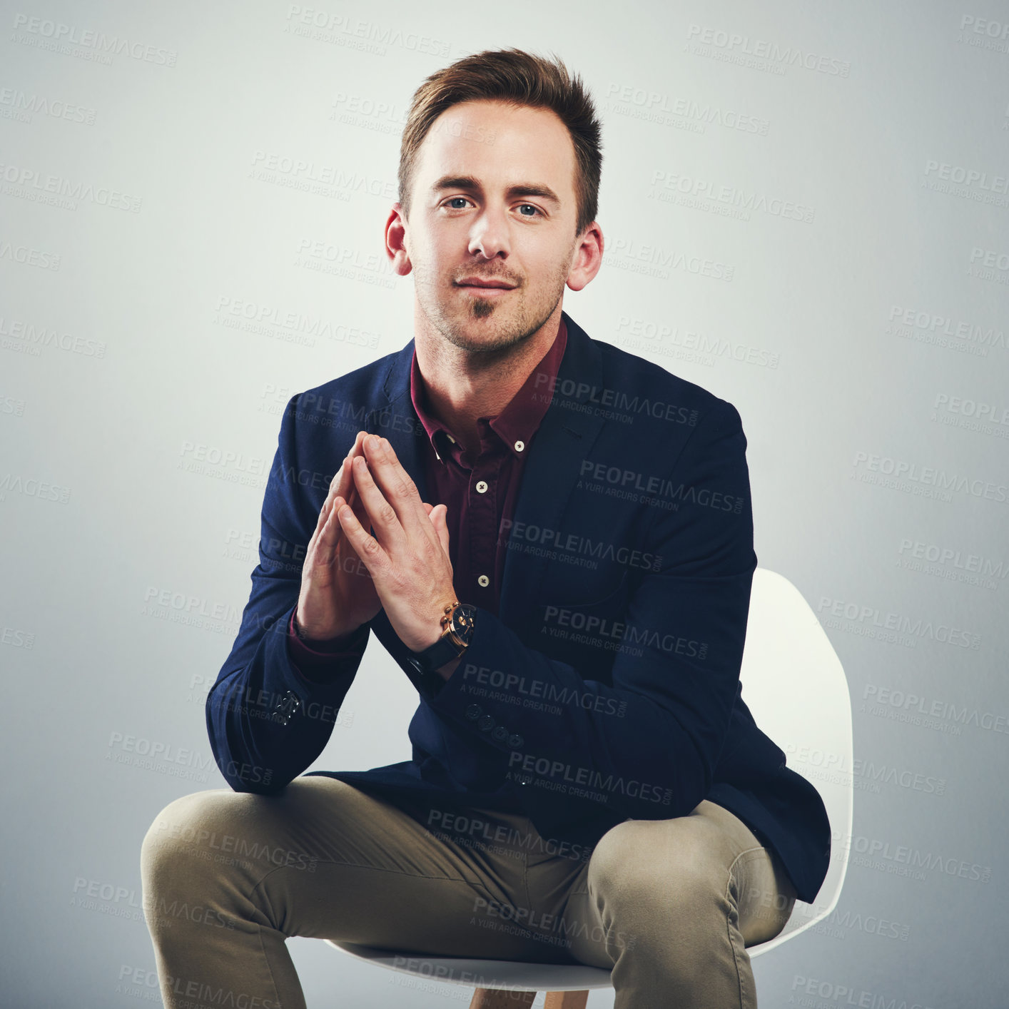 Buy stock photo Studio portrait of a confident young businessman sitting on a chair against a gray background