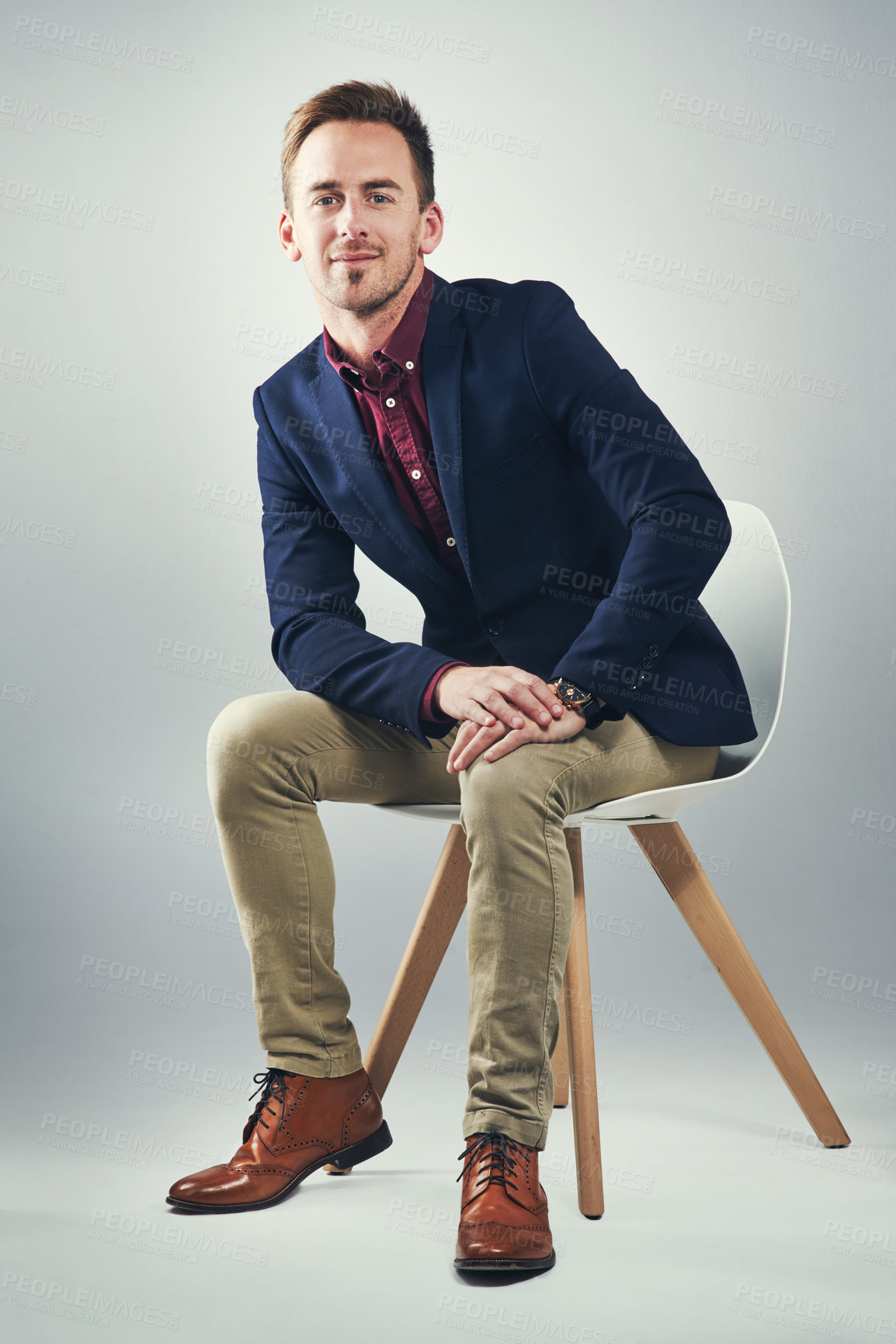 Buy stock photo Studio portrait of a confident young businessman sitting on a chair against a gray background