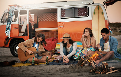 Buy stock photo Shot of a group of friends sitting around a fire on the beach