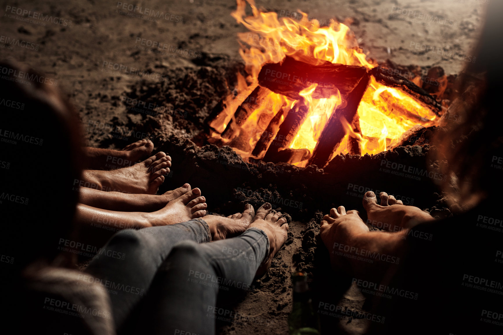 Buy stock photo Cropped shot of a group of unrecognizable friends sitting around a bonfire on the beach at night
