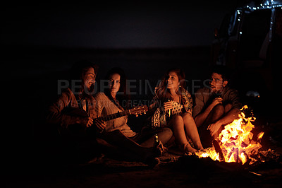 Buy stock photo Shot of a group of friends sitting around a bonfire on the beach at night