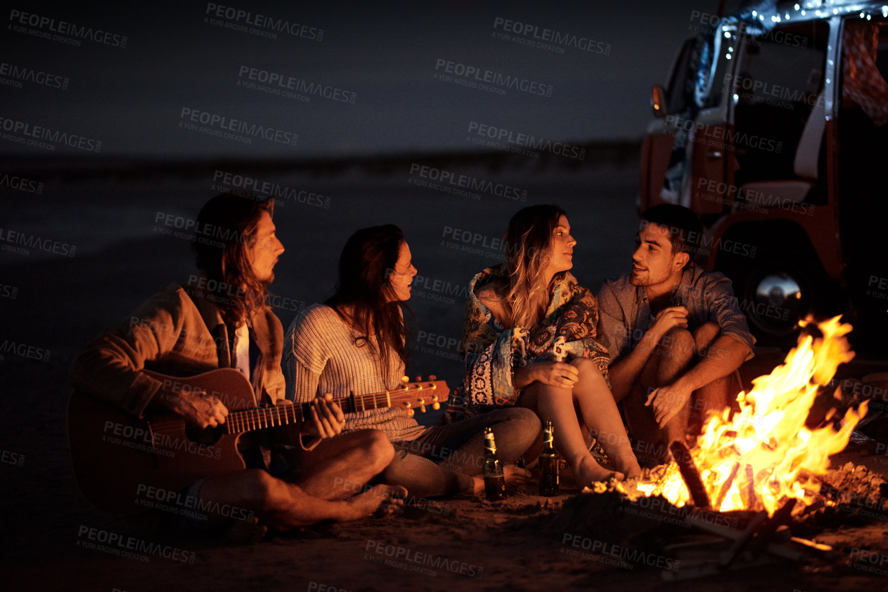 Buy stock photo Shot of a group of friends sitting around a bonfire on the beach at night