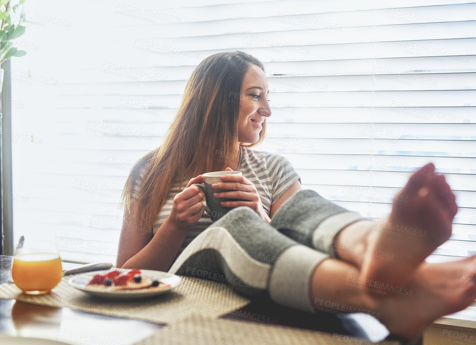 Buy stock photo Cropped shot of a young woman having breakfast and chilling by the dining table in the morning at home