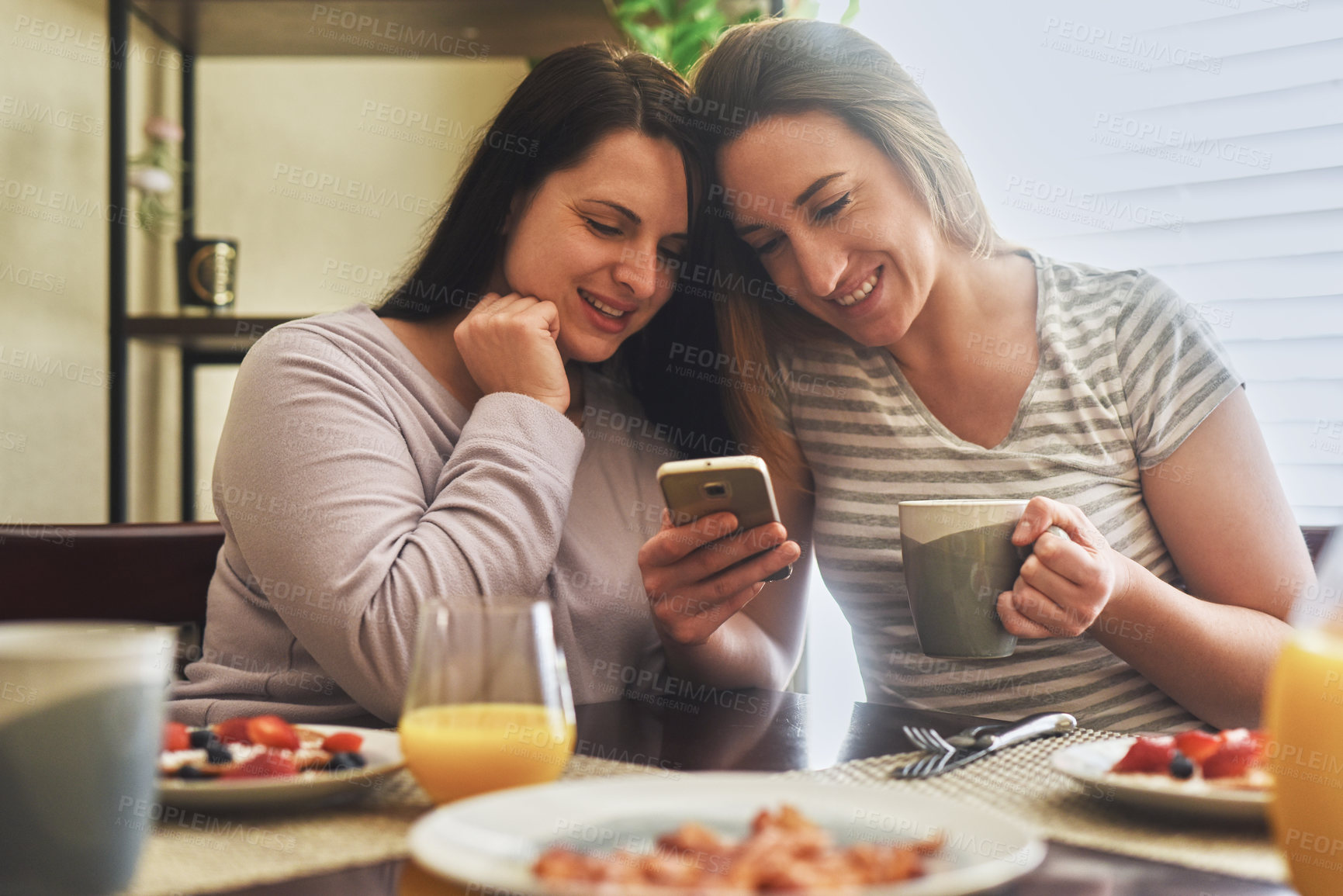 Buy stock photo Cropped shot of two young women using a cellphone together while having breakfast in the morning at home