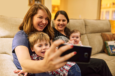 Buy stock photo Cropped shot of two mothers taking a selfie with their adorable children on the couch at home
