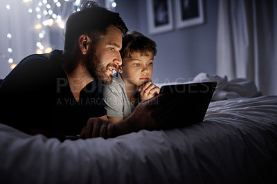 Buy stock photo Shot of a father and his little son using a digital tablet together in bed at night