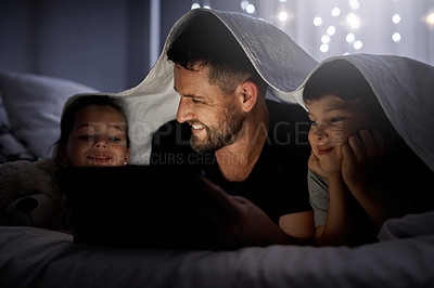 Buy stock photo Shot of a father and his two little children using a digital tablet together in bed at night