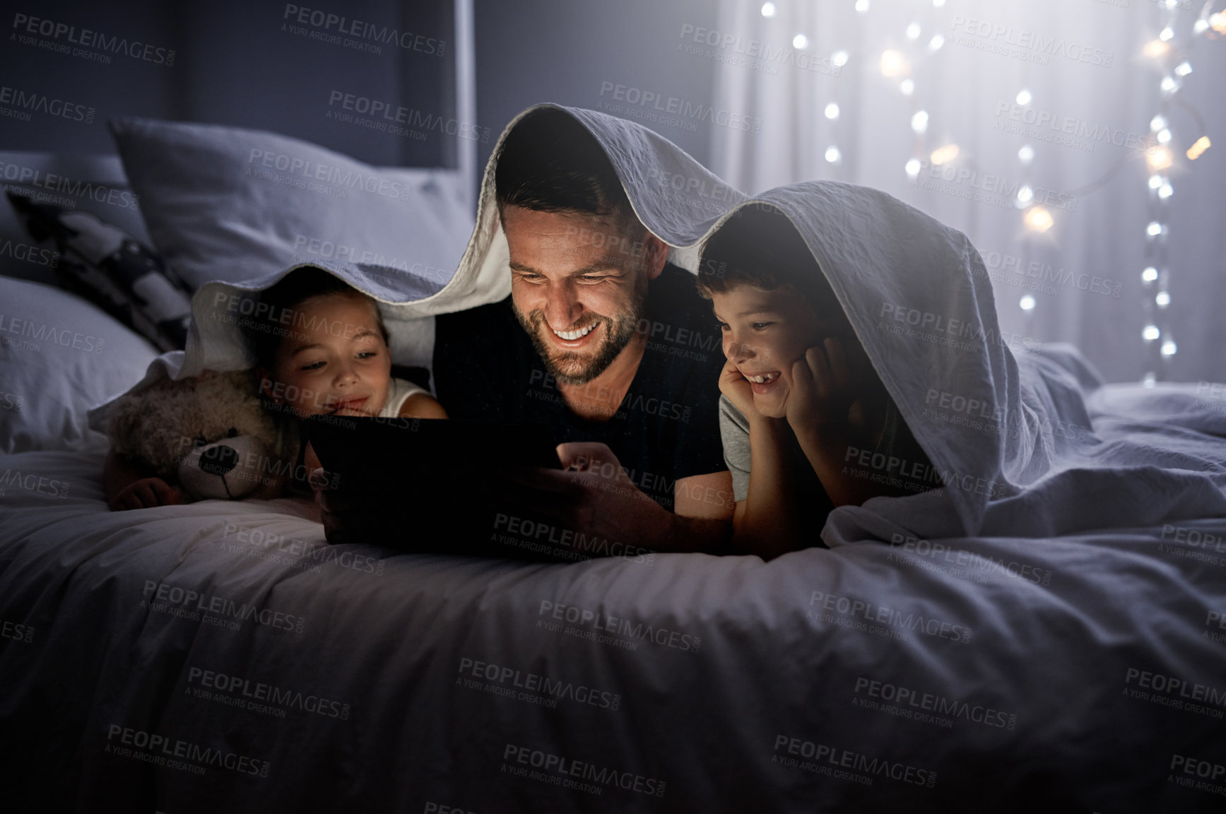 Buy stock photo Shot of a father and his two little children using a digital tablet together in bed at night