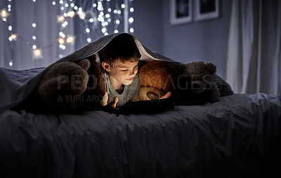 Buy stock photo Shot of an adorable little boy using a digital tablet in bed at night