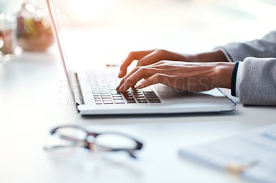 Buy stock photo Businesswoman typing work on a laptop at her desk in a modern office. Busy female doing business on keyboard working with reports, documents and emails or browsing the internet at the workplace.