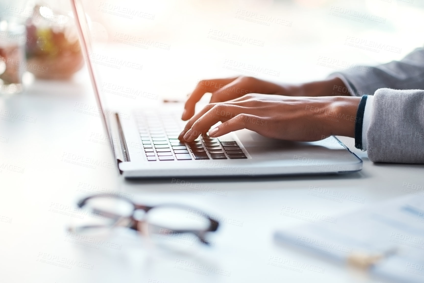 Buy stock photo Businesswoman typing work on a laptop at her desk in a modern office. Busy female doing business on keyboard working with reports, documents and emails or browsing the internet at the workplace.