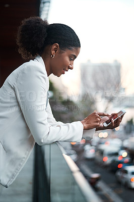 Buy stock photo Relaxed business woman texting on her phone while standing on a balcony on her lunch break. Young corporate female browsing the internet or scrolling on social media after work in a city