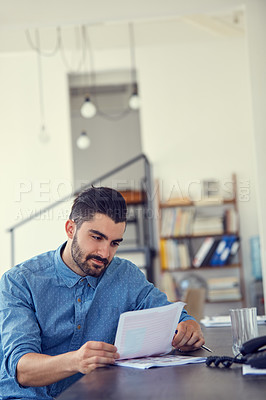 Buy stock photo Shot of a young businessman working through paperwork her desk in a modern office