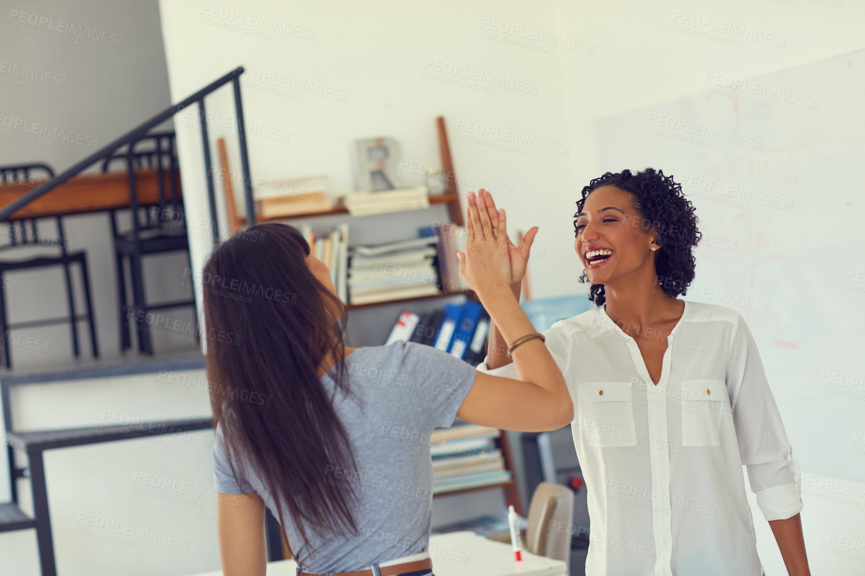 Buy stock photo Shot of two young businesswomen giving each other a high five in a modern office