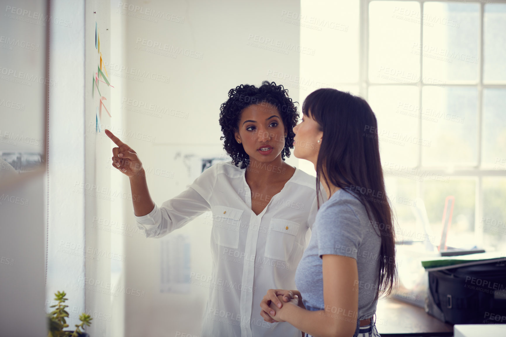 Buy stock photo Shot of two young businesswomen having a brainstorming session on a wall in a modern office