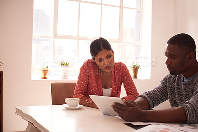 Buy stock photo Shot of a young businessman and businesswoman using a digital tablet while discussing paperwork in a modern office