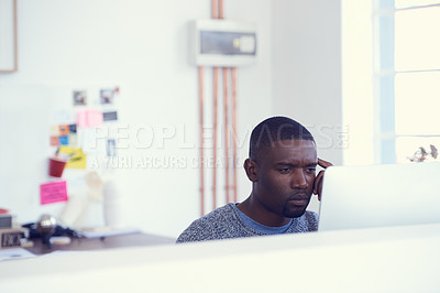 Buy stock photo Shot of a young businessman looking serious while using a computer in a modern office