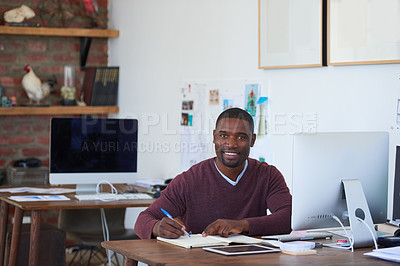 Buy stock photo Portrait of a young businessman writing notes at his desk in a modern office