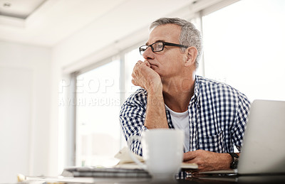 Buy stock photo Shot of a mature man looking thoughtful while working on a laptop at home
