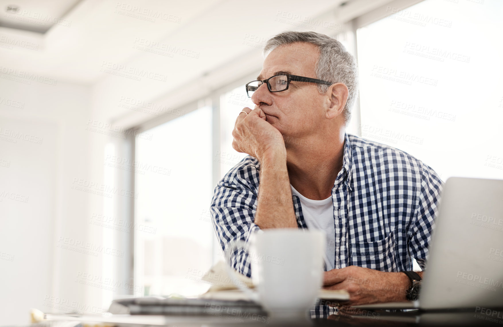 Buy stock photo Shot of a mature man looking thoughtful while working on a laptop at home