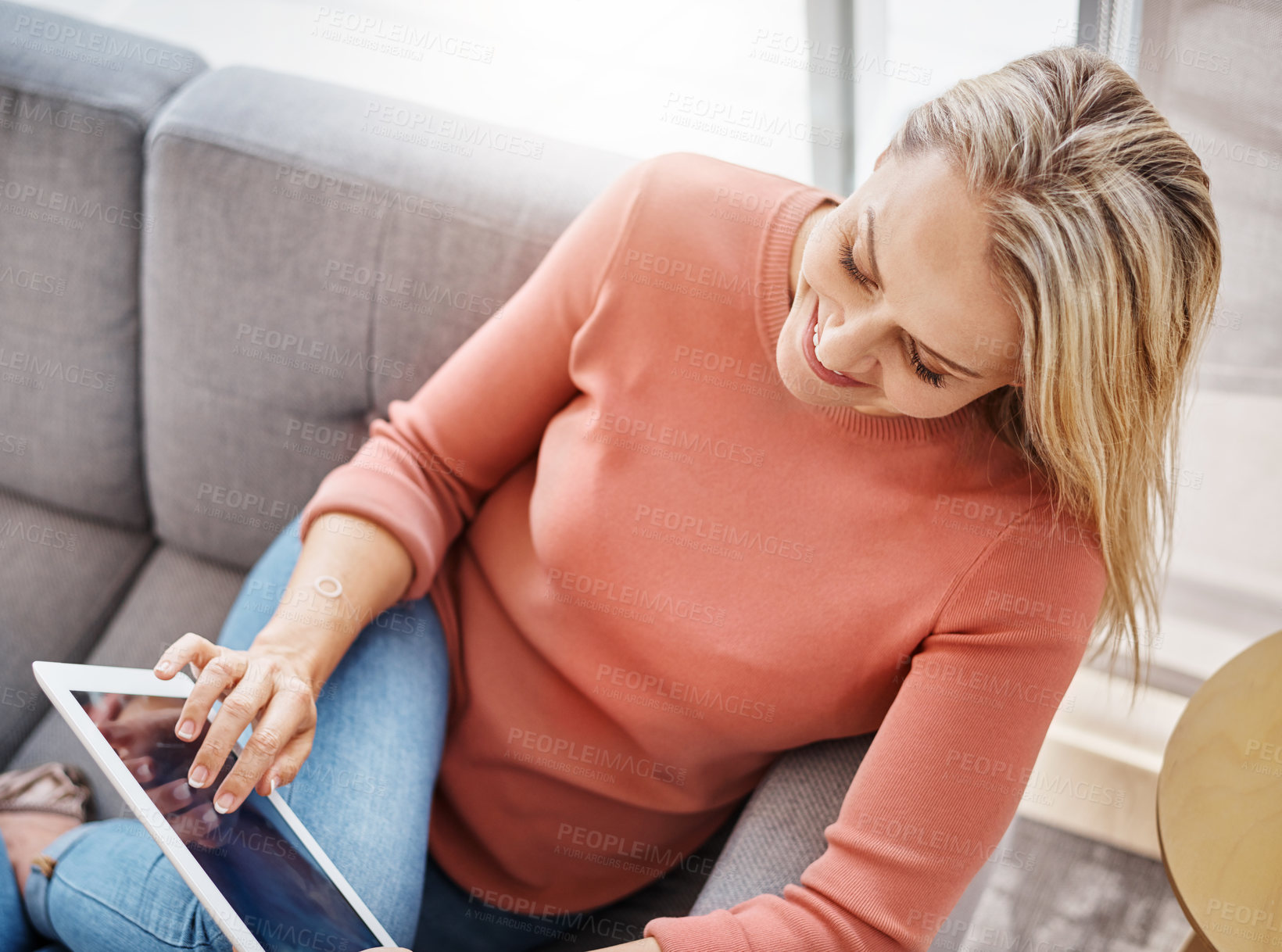 Buy stock photo Shot of an attractive mature woman using a digital tablet while relaxing on the sofa at home