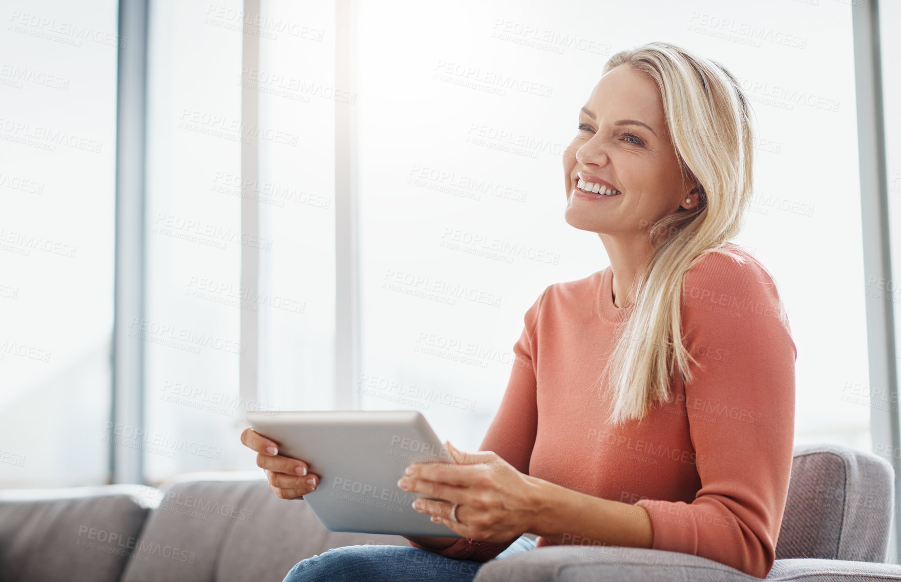 Buy stock photo Shot of an attractive mature woman using a digital tablet while relaxing on the sofa at home
