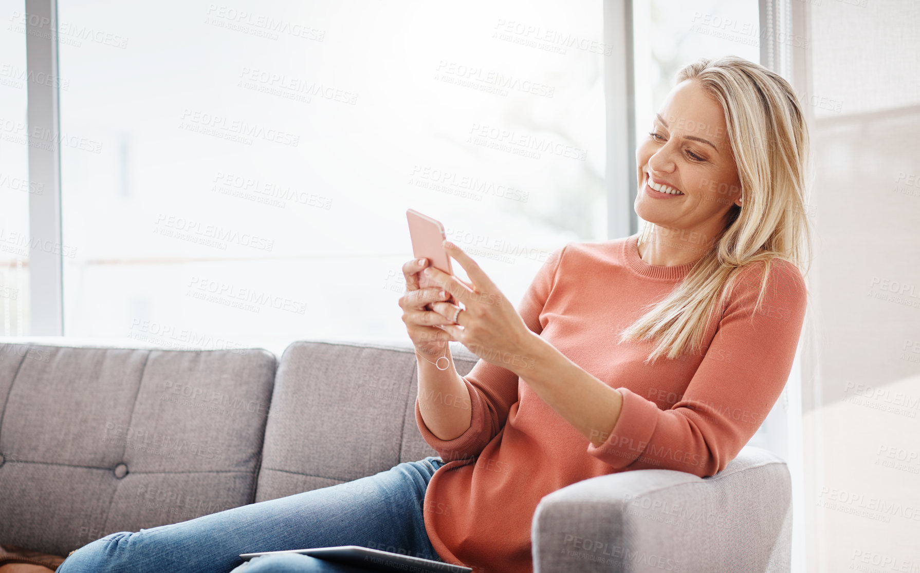 Buy stock photo Shot of an attractive mature woman using a mobile phone while relaxing on the sofa at home