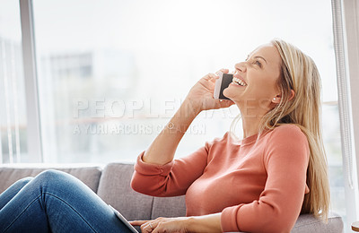 Buy stock photo Shot of an attractive mature woman using a mobile phone and digital tablet while relaxing on the sofa at home